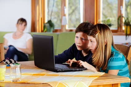children at the laptop with mother in the background