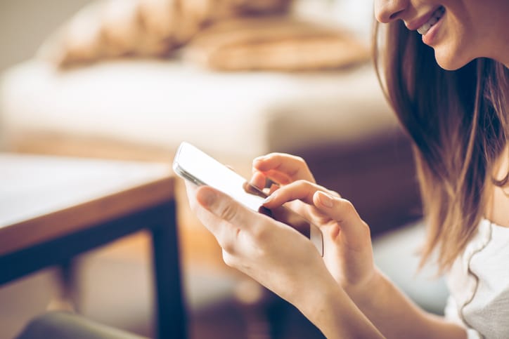 Young happy woman typing on smart phone